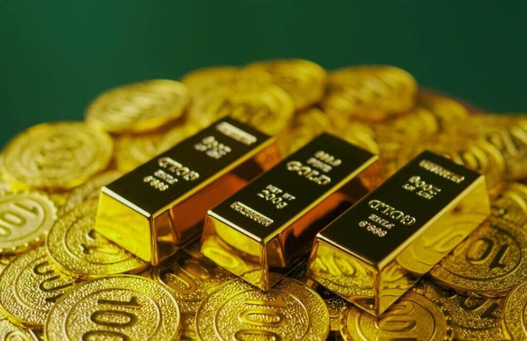 Gestapelte 999,9er Feingoldbarren auf Goldmünzen, die langfristigen Vermögenserhalt, finanzielle Sicherheit und Inflationsschutz symbolisieren